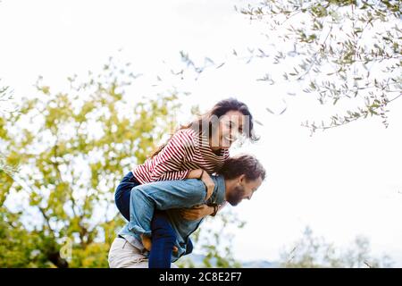 Giocoso uomo piggybacking allegra ragazza contro il cielo Foto Stock