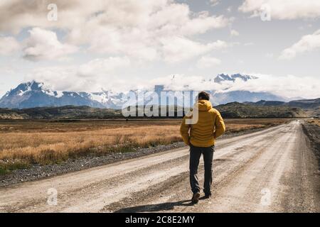 Uomo maturo che cammina su strada sterrata contro il cielo nuvoloso, Parco Nazionale Torres del Paine, Patagonia, Cile Foto Stock