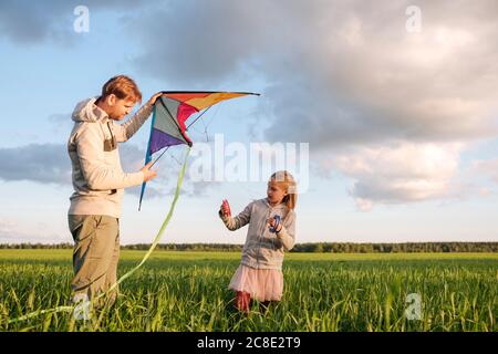 Padre e figlia volano aquilone mentre si levano in piedi sul paesaggio verde contro il cielo Foto Stock