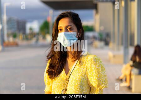 Giovane donna che indossa la maschera mentre si sta in piedi sulla strada della città Foto Stock
