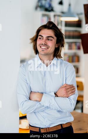 Sorridente professionista maschile con braccia incrociate in piedi da parete caffetteria Foto Stock