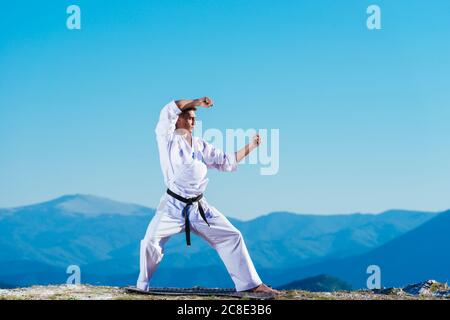 Bionda atleta di karate non kata sulla cima di una montagna mentre si esegue una linea di calci, pugni e blocchi sulla cima di una montagna in una giornata di sole. Foto Stock