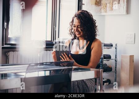 Sorridendo bella giovane donna che usa il tablet digitale mentre si siede a. tavolo da pranzo Foto Stock
