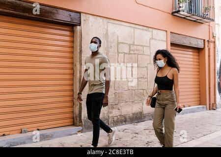 Uomo e donna indossano maschere mentre camminano sulla strada della città Foto Stock