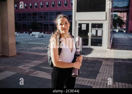 Giovane donna sportiva che tiene il tappetino per esercizi mentre si trova in città via Foto Stock