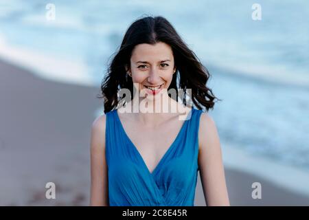 Donna Darkhaired in abito blu camminando sulla spiaggia, sorridente, ritratto Foto Stock