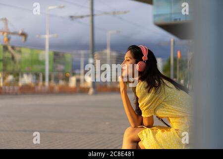 Giovane donna premurosa che ascolta la musica mentre si siede in città Foto Stock