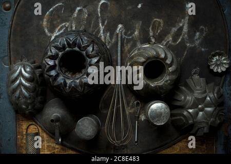 Collezione di vecchi utensili da cucina rustici tra cui teglie, teglia da forno, grattugia, frusta e imbuto Foto Stock