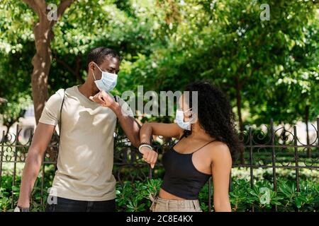 Uomo e donna indossando maschere mentre si salutano l'un l'altro toccare i gomiti al parco Foto Stock