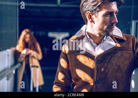 Uomo d'affari premuroso in attesa all'aeroporto con donna in background Foto Stock