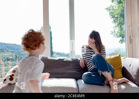 Ragazzo che corre verso la madre seduto con gli occhi di copertura della mano a. casa Foto Stock