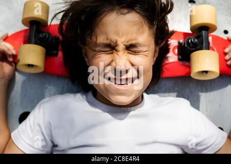 Primo piano di ragazzo con gli occhi chiusi facendo faccia mentre si sdraiava su skateboard Foto Stock