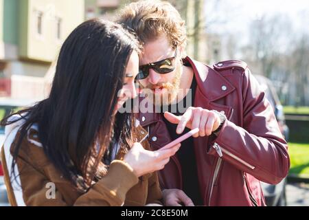 Primo piano di una giovane coppia che utilizza lo smartphone mentre si è seduti all'aperto il giorno di sole Foto Stock