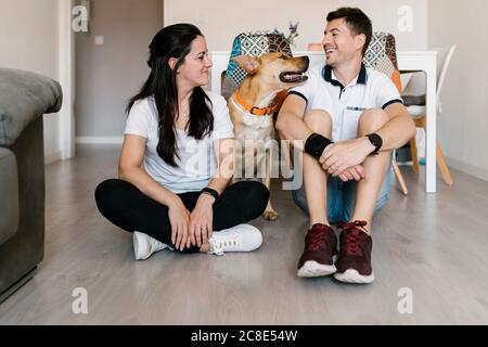 Coppia sorridente che si diverta con il cane mentre si siede sul pavimento a. casa Foto Stock