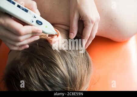 Fisioterapista che usa stimolatore di punti di agopuntura sull'orecchio della femmina paziente Foto Stock