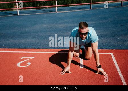 Atleta maschile in posizione di partenza sulla pista di tartan Foto Stock