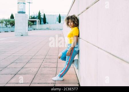 Giovane donna sorridente appoggiata al muro Foto Stock