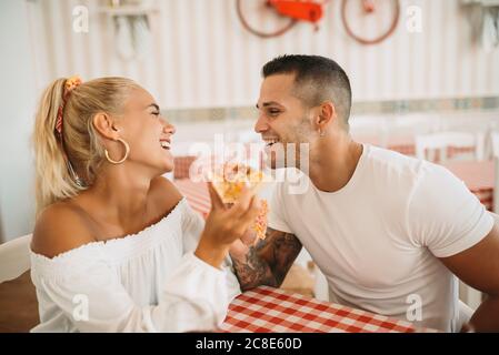 Felice giovane coppia che mangia pizza mentre si siede al ristorante Foto Stock