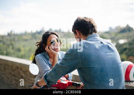 Donna felice che indossa occhiali da sole che parla con il ragazzo seduto su Vespa Foto Stock