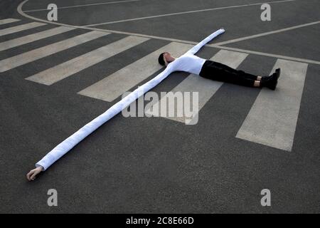 Donna con lunghe mani artificiali sdraiata sul crosswalk Foto Stock