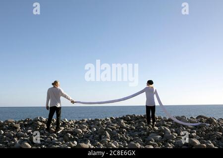 Donna con braccia lunghe che tiene la mano dell'uomo in spiaggia contro cielo limpido Foto Stock