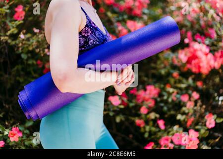 Indossate la donna con il tappetino viola per yoga mentre siete in piedi nel parco Foto Stock