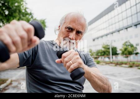 Primo piano di un uomo anziano sicuro che tiene i manubri mentre si sta in piedi città Foto Stock