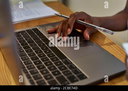 Mano tagliata di donna che usa il computer portatile sul tavolo mentre studia a casa Foto Stock