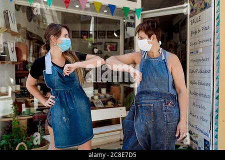 Le donne che indossano maschere che danno il gomito a battuta mentre si levano in piedi contro officina Foto Stock