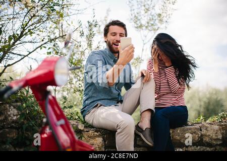 Uomo felice che usa lo smartphone mentre si siede con la ragazza parete di ritegno Foto Stock