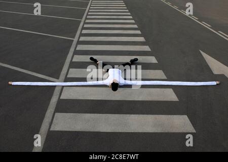 Donna con lunghe mani artificiali distesi gambe a parte sul crosswalk Foto Stock