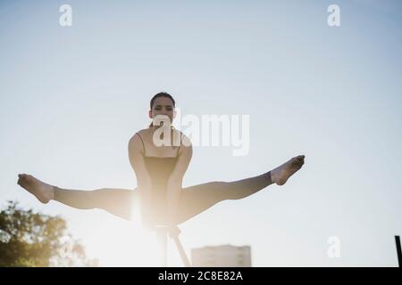 Donna giovane e sicura che esegue il sostegno a mano sulla ringhiera contro il cielo limpido durante il giorno di sole Foto Stock