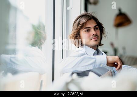 Uomo d'affari premuroso che guarda lontano mentre si siede vicino alla finestra nel caffè Foto Stock