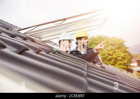 Due uomini che indossano cappelli duri che guardano fuori dalla finestra del tetto Foto Stock