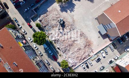 Vista aerea dell'escavatore demolisce un vecchio edificio nel centro della città. Il calcestruzzo distrutto viene caricato sul carrello Foto Stock