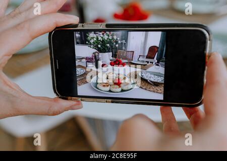 Primo piano di una donna che fotografa cheesecake e fragole sul tavolo da pranzo a casa Foto Stock