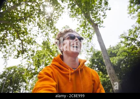 Ritratto di giovane ridente che indossa occhiali da sole e felpa con cappuccio arancione camicia in natura Foto Stock