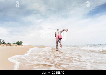 Vista posteriore di un atletico che corre sulla spiaggia Foto Stock