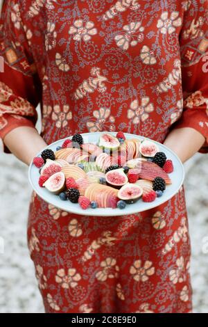 Primo piano di una giovane donna che tiene i frutti in tavola mentre si sta in piedi all'aperto Foto Stock