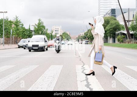 Ragazza teenage musulmana che parla attraverso lo smartphone mentre si attraversa la strada in città Foto Stock