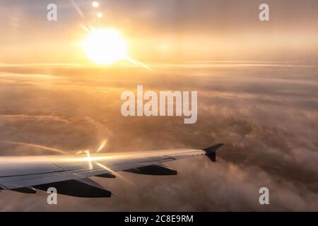 Vista sull'ala destra dell'aeromobile per passeggeri. Il tramonto splende come una palla di luce dorata sull'ala. Le nubi spesse sotto l'aereo sono illuminate dai dorati s. Foto Stock