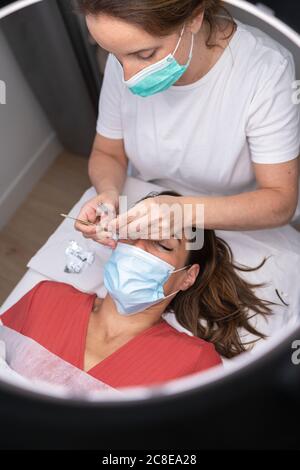 Beautician femminile maturo usando gli attrezzi manuali per l'estensione del ciglia sopra cliente Foto Stock