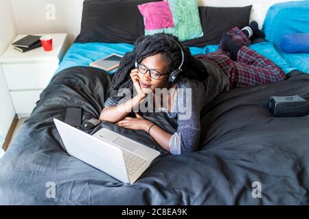 Giovane donna che usa un computer portatile per guardare film a letto a casa Foto Stock