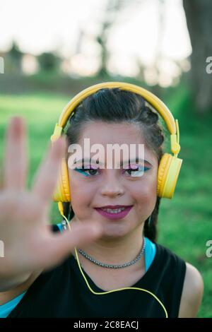 Adolescente ragazza con sindrome di Down indossare 8s trucco colorato e. ascolto di musica con le cuffie gialle Foto Stock