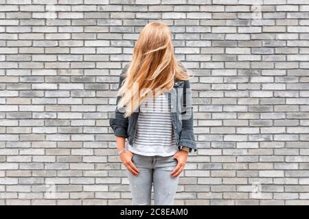 Donna con capelli davanti al viso in piedi contro il grigio muro di mattoni Foto Stock