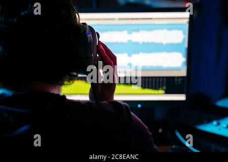 Uomo che tiene le cuffie mentre usa il computer in studio di registrazione a. casa Foto Stock