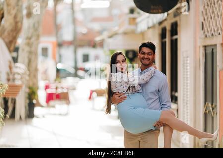 Uomo felice che porta una donna incinta in città durante il giorno di sole Foto Stock