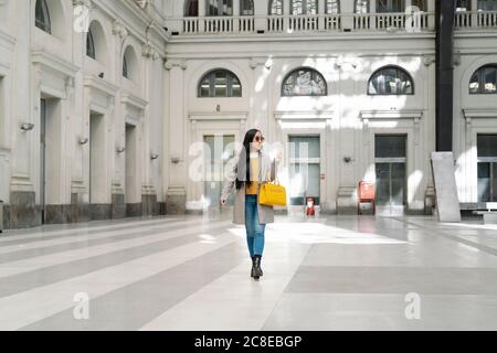 Giovane donna elegante che cammina sul pavimento contro l'edificio Foto Stock