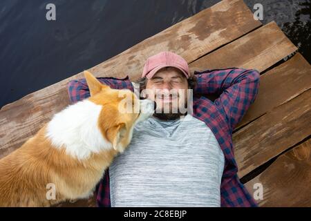 Uomo rilassato sdraiato sul lungomare con il cane a riva del fiume Foto Stock