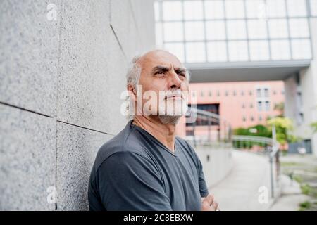 Primo piano di un uomo senior attento che guarda lontano mentre si sta in piedi parete Foto Stock